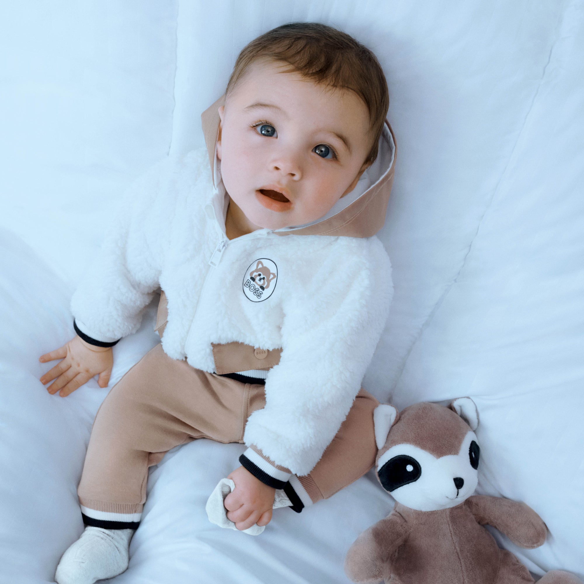 Baby in Hugo Boss jacket with plush toy raccoon