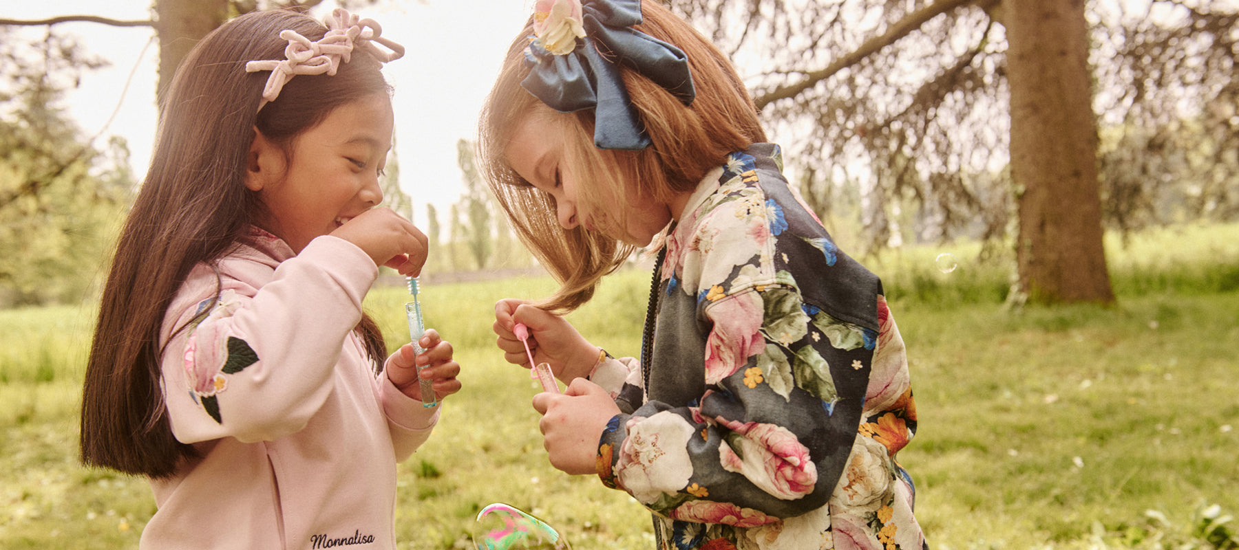 Two children in Monnalisa fashions blowing bubble in the park