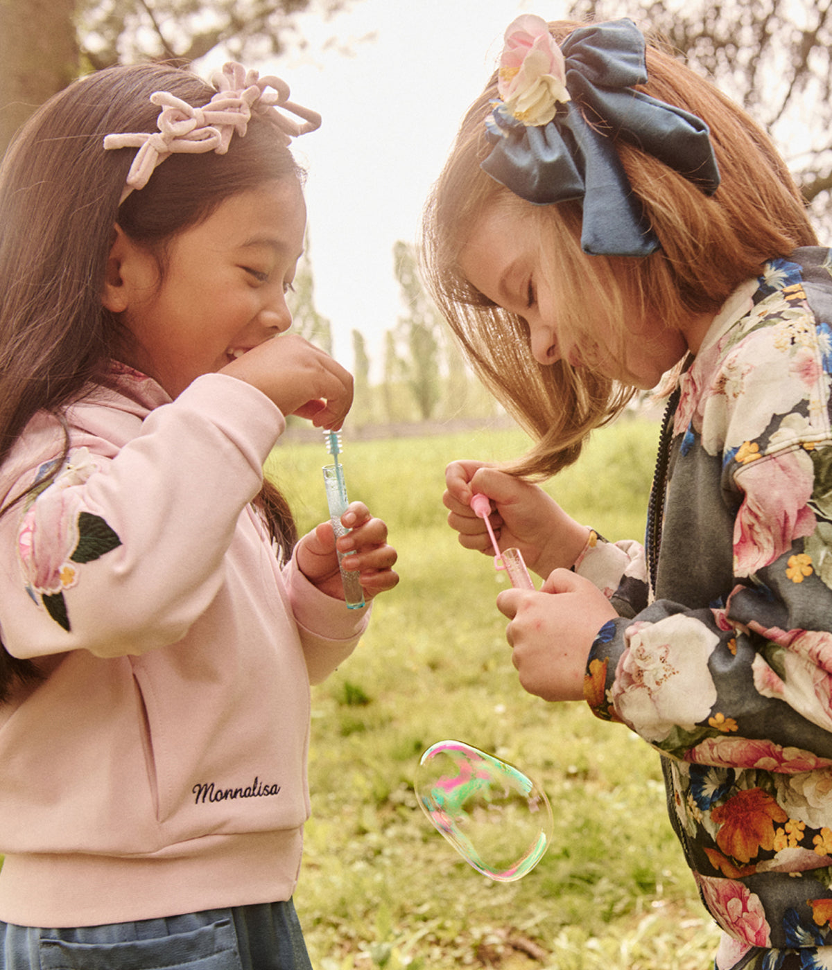 Two children in Monnalisa fashions blowing bubble in the park